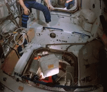 A Man Sits In A Space Station With A Sign That Says To Lab And To Hab GIF