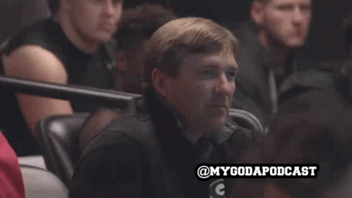 a man sits in a stadium watching a game with the hashtag mygodapodcast