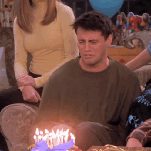 A Man Sits In Front Of A Birthday Cake With Candles GIF