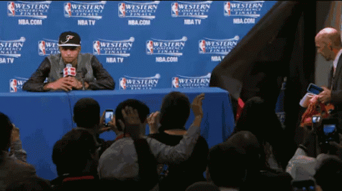A Man Sits In Front Of A Wall That Says Western Conference Finals On It GIF
