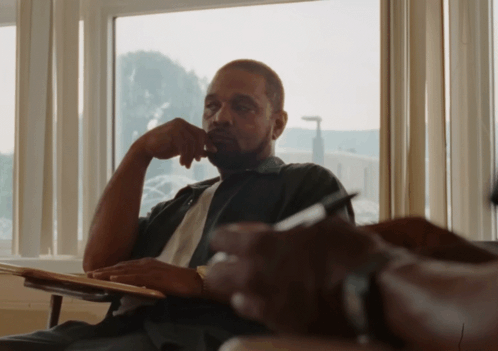 A Man Sits In Front Of A Window With His Hand To His Chin GIF
