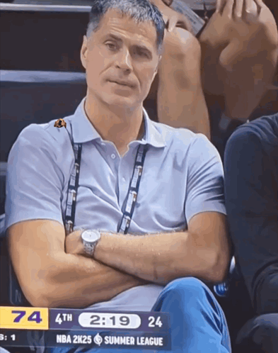 a man sits in the stands with his arms crossed and a nba 2k25 summer league scoreboard in the background