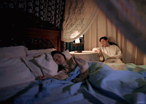 A Man Sits Next To A Woman Sleeping In A Bed With The Name Kamikaze On The Bottom Right Corner GIF