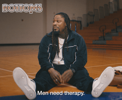 A Man Sits On A Basketball Court With The Words Men Need Therapy Above Him GIF