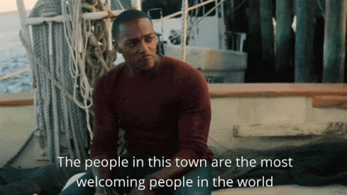 A Man Sits On A Boat With The Words " The People In This Town Are The Most Welcoming People In The World " Below Him GIF