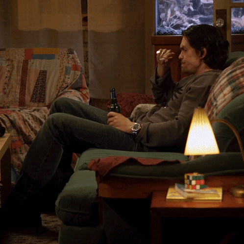 A Man Sits On A Couch Drinking A Beer GIF