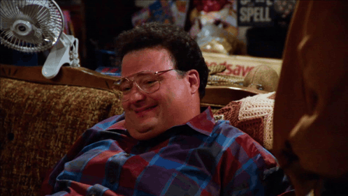 A Man Sits On A Couch Next To A Sign That Says " Spell " GIF