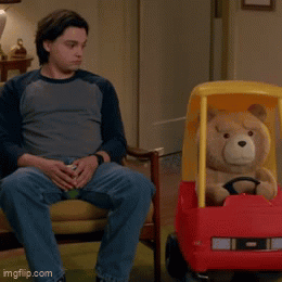 A Man Sits On A Couch Next To A Teddy Bear In A Cozy Coupe GIF