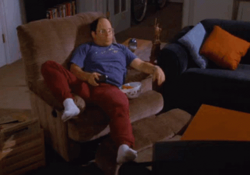A Man Sits On A Couch With A Shelf Full Of Cans And Snacks GIF