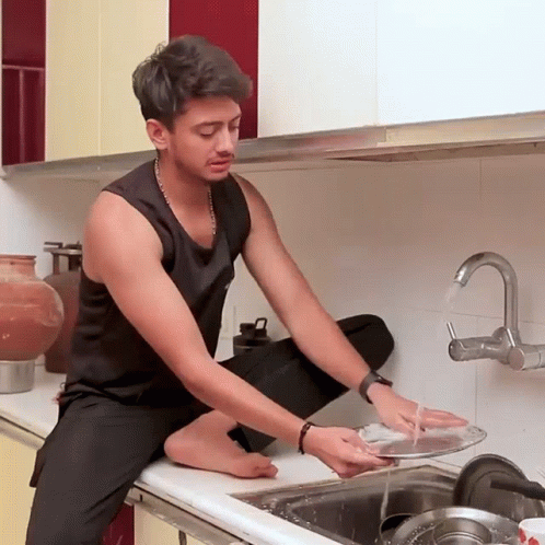 A Man Sits On A Counter Washing Dishes In A Kitchen GIF