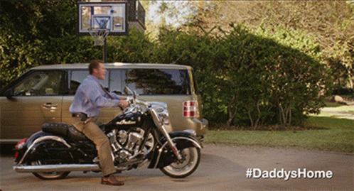 a man sits on a motorcycle in front of a van and a basketball hoop with the hashtag #daddyshome