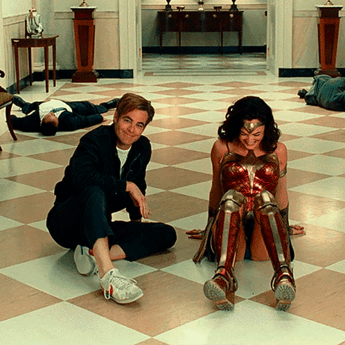 A Man Sits On The Floor Next To A Woman In A Wonder Woman Outfit GIF