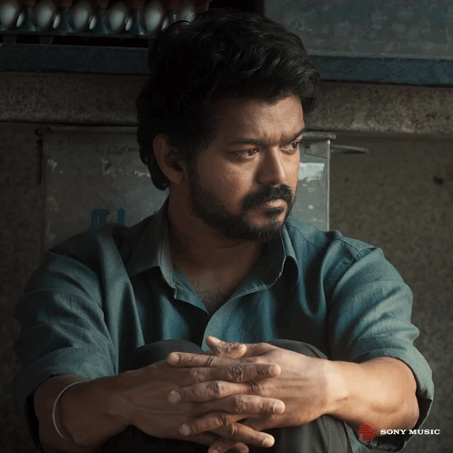 A Man Sits With His Hands Folded In Front Of A Sony Music Ad GIF