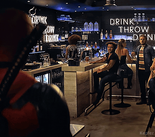 A Man Sitting At A Bar With A Sign That Says Drink Throw Drink GIF
