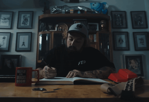 A Man Sitting At A Desk Wearing A Black Ftp Shirt GIF