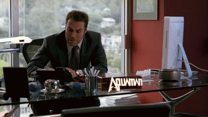 A Man Sitting At A Desk With A Sign That Says Aquafina GIF