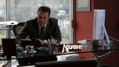 A Man Sitting At A Desk With A Sign That Says Aquafina GIF