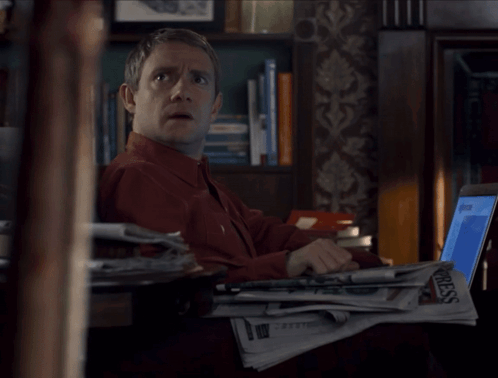 A Man Sitting At A Desk With A Stack Of Newspapers And A Laptop With The Word Press On It GIF