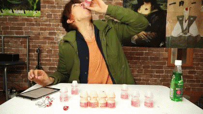 A Man Sitting At A Table Drinking From A Bottle That Says Sprite On It GIF