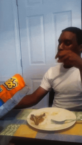 A Man Sitting At A Table Eating A Bag Of Cheetos GIF
