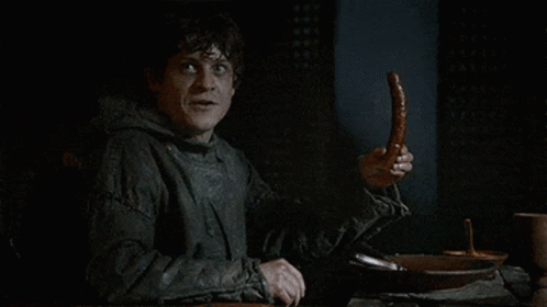 A Man Sitting At A Table Holding A Sausage In His Hand . GIF