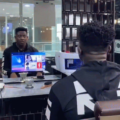 A Man Sitting At A Table Looking At A Computer Screen That Says Facebook GIF