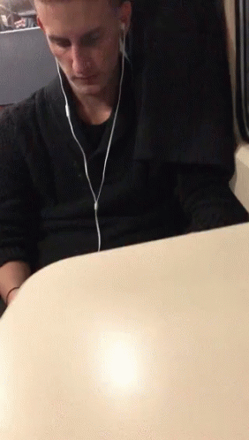 A Man Sitting At A Table Wearing Ear Buds GIF