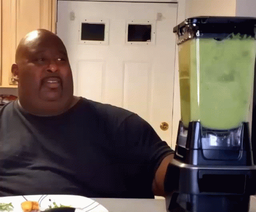 A Man Sitting At A Table With A Blender In Front Of Him GIF