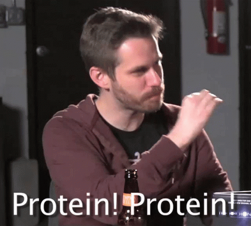 A Man Sitting At A Table With A Bottle Of Beer And A Sign That Says Protein Protein GIF