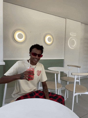 A Man Sitting At A Table With A Drink In His Hand GIF
