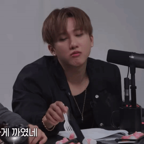 A Man Sitting At A Table With A Fork In His Hand And A Microphone In The Background GIF