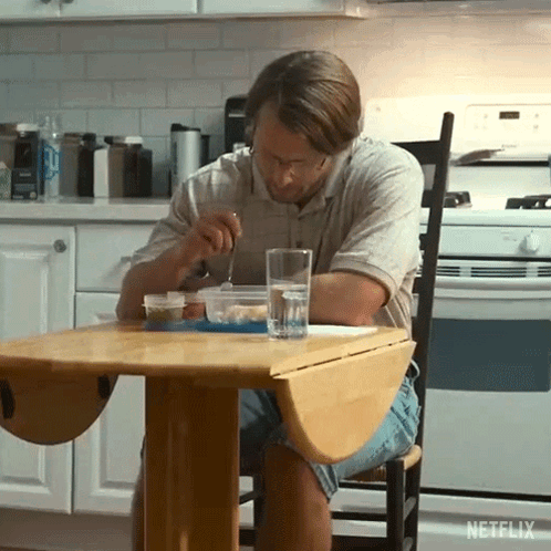 A Man Sitting At A Table With A Glass Of Water And A Bowl Of Food GIF