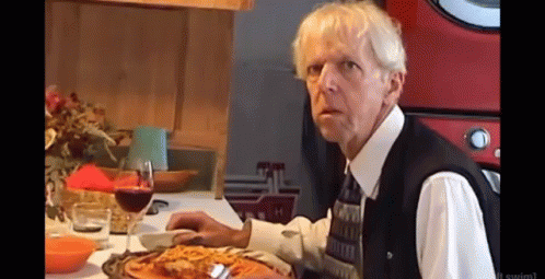 A Man Sitting At A Table With A Glass Of Wine And A Plate Of Pizza GIF
