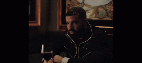 A Man Sitting At A Table With A Glass Of Wine In His Hand GIF