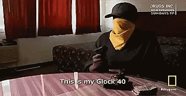 A Man Sitting At A Table With A Gun And Says This Is My Glock 40 GIF