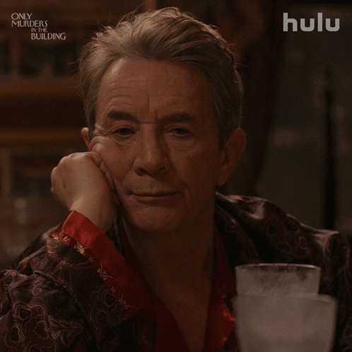 A Man Sitting At A Table With A Hulu Logo Behind Him GIF