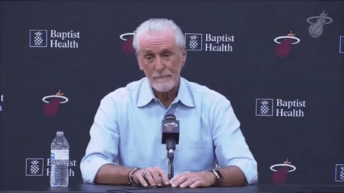 A Man Sitting At A Table With A Microphone In Front Of A Wall That Says Baptist Health GIF