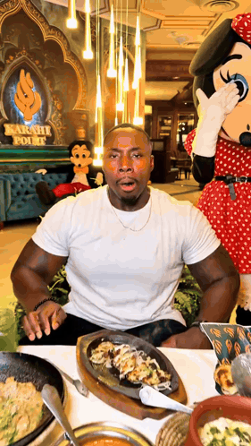 a man sitting at a table with a minnie mouse mascot covering his mouth