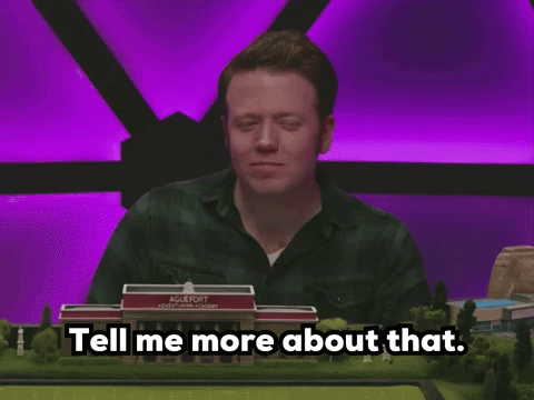 A Man Sitting At A Table With A Model Of A School Behind Him And The Words Tell Me More About That GIF