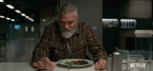 A Man Sitting At A Table With A Plate Of Food And A Netflix Logo On The Bottom GIF