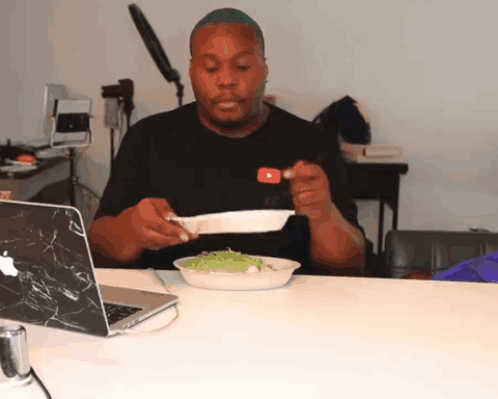 a man sitting at a table with a plate of food in front of a laptop