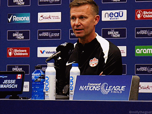 A Man Sitting At A Table With A Sign That Says Nations League Finals GIF