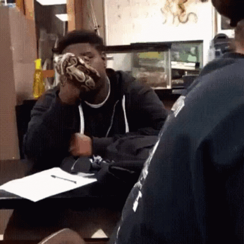 A Man Sitting At A Table With A Snake On His Face GIF