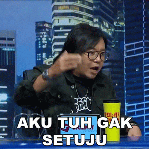 A Man Sitting At A Table With A Yellow Cup That Says Aku Tuh Gak Setuju On It GIF