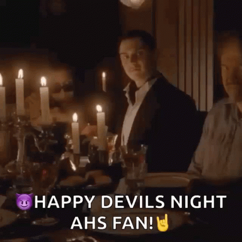 A Man Sitting At A Table With Candles And The Words Happy Devils Night Ahs Fan On The Bottom GIF