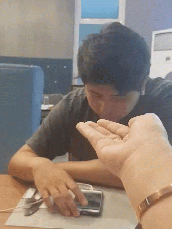 A Man Sitting At A Table With His Hand On A Phone GIF