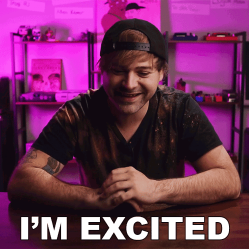 A Man Sitting At A Table With The Words " I 'M Excited " Written On The Screen GIF
