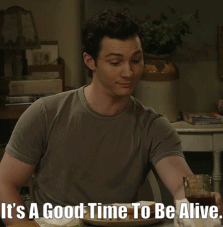 A Man Sitting At A Table With The Words It 'S A Good Time To Be Alive On The Bottom GIF