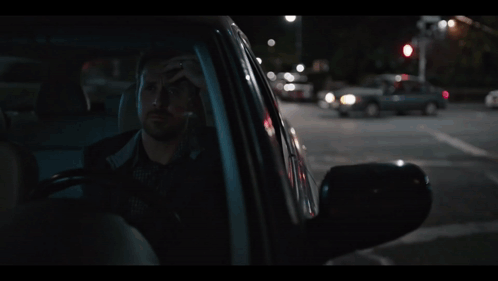 A Man Sitting In A Car With His Head In His Hand GIF