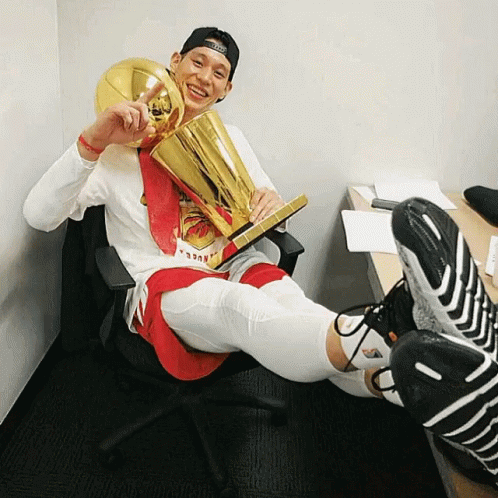 A Man Sitting In A Chair Holding A Trophy That Says ' Nba ' On It GIF